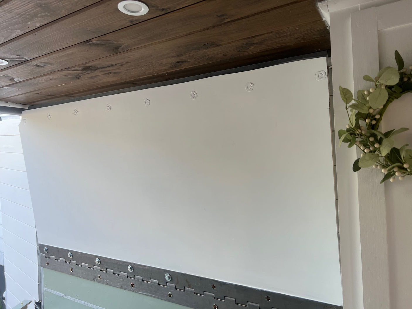 RV rental interior: A white hinged panel with circular fasteners, a wood plank ceiling, and a decorative wreath.
