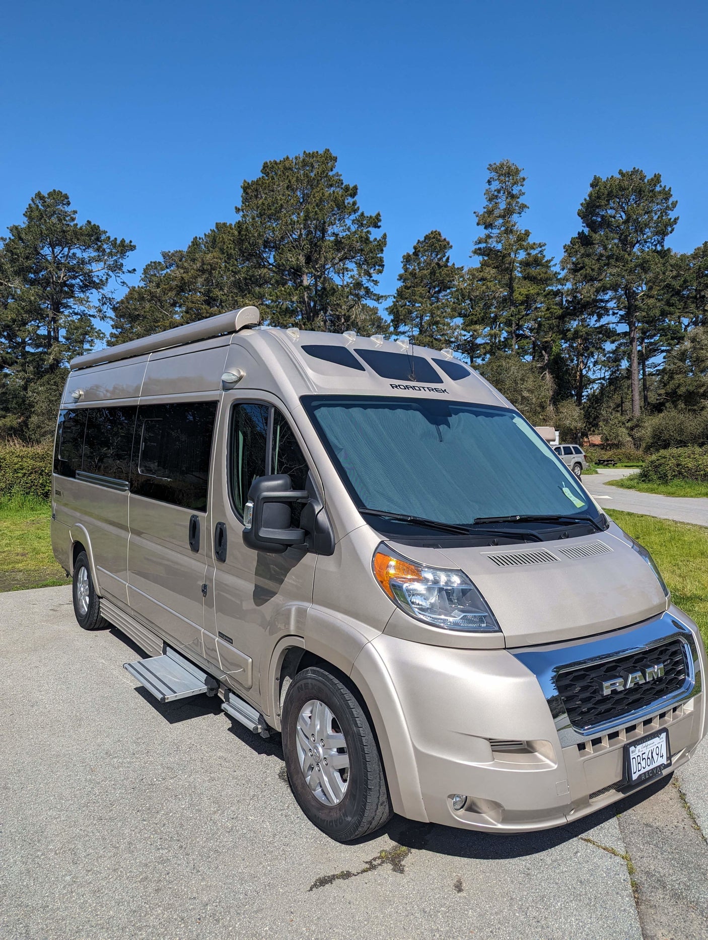 Gold Roadtrek camper van with steps extended, parked under a clear blue sky. Perfect for an RV rental.