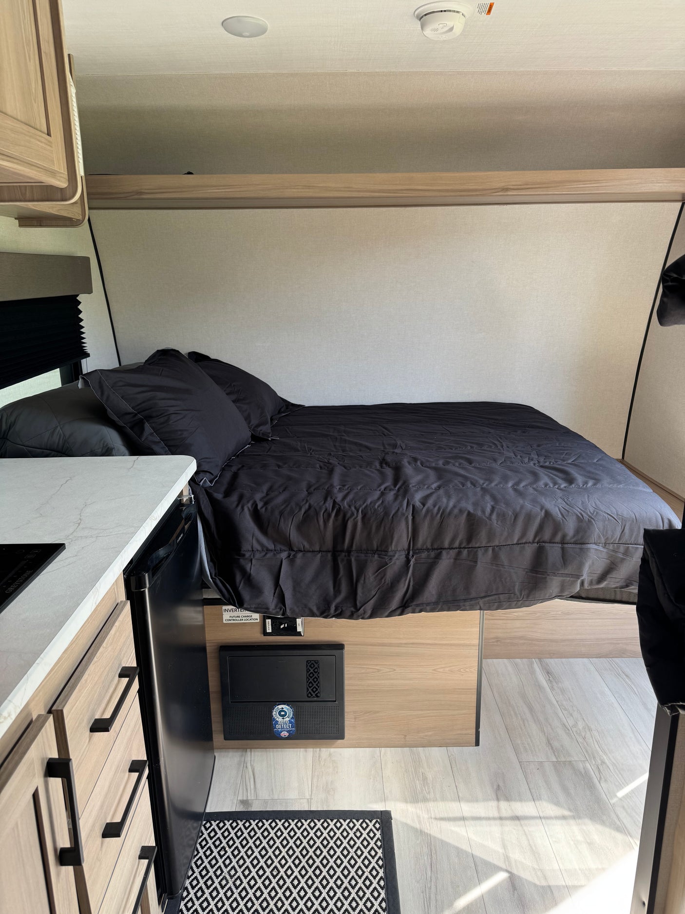 Comfortable RV rental interior: bedroom with black bedding, compact kitchen, light wood accents. Perfect for travel!