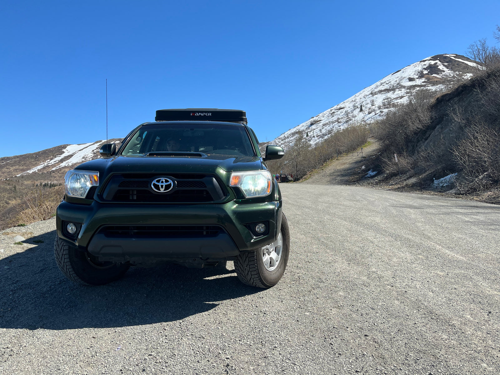 A green Toyota truck with an iKamper rooftop tent on a mountain road, ideal for an RV rental camping adventure.