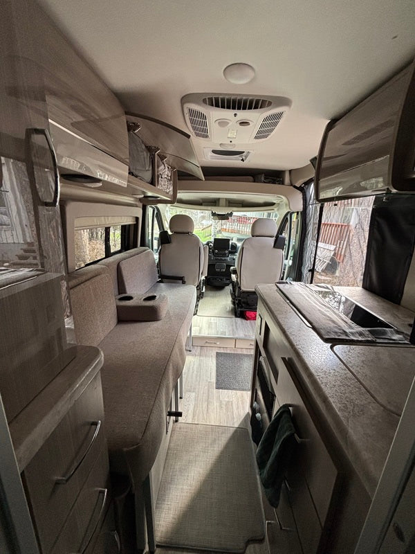 Looking forward inside a sleek rv rental camper van, revealing a compact kitchen, seating, and overhead storage.