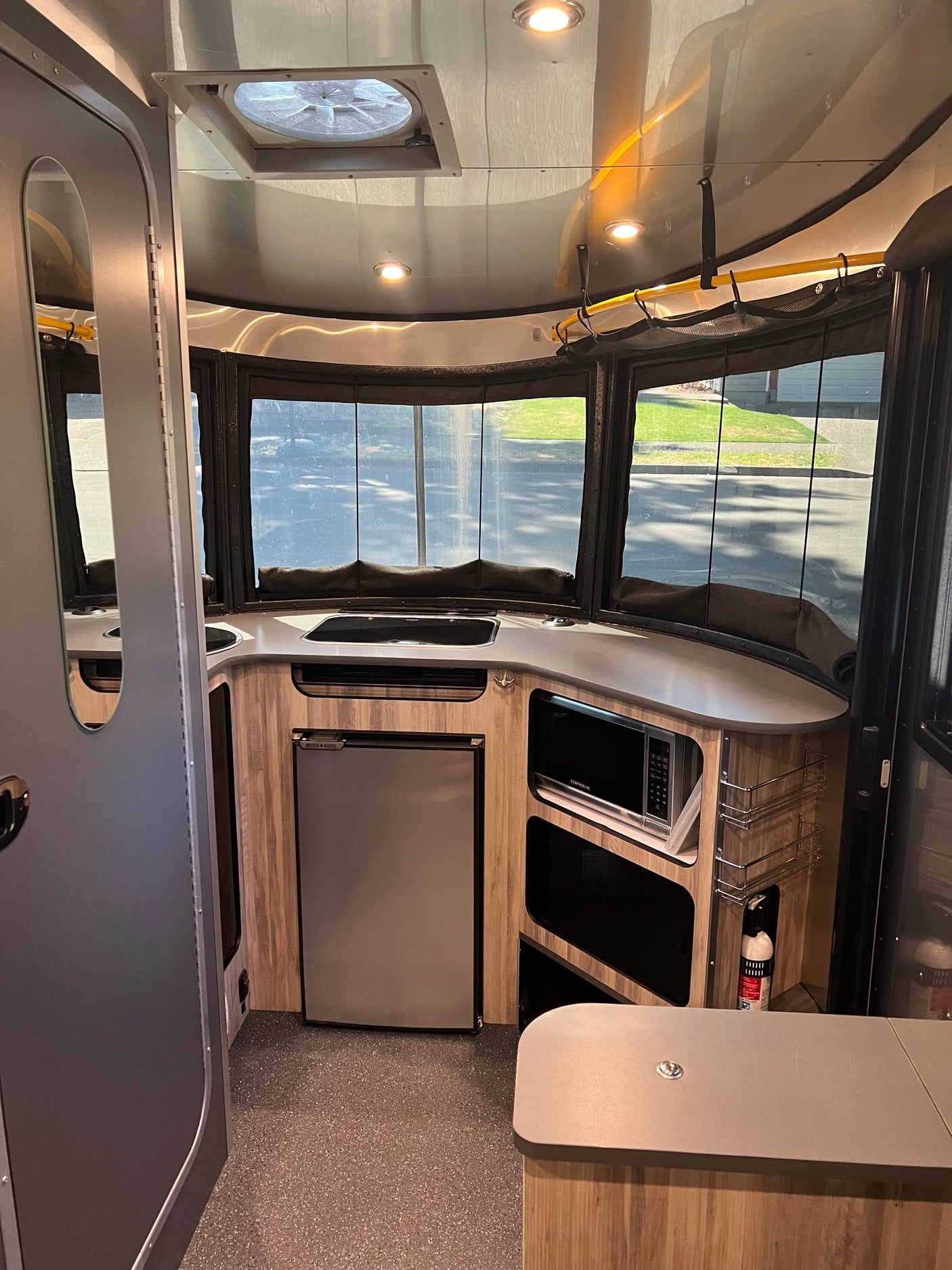 Compact RV rental interior featuring a kitchen with sink, microwave, and fridge, plus large windows for scenic views.
