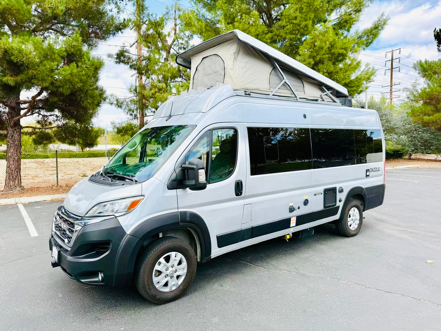 A sleek silver pop-top camper van, available for rv rental, is parked outdoors. Features a raised roof tent.