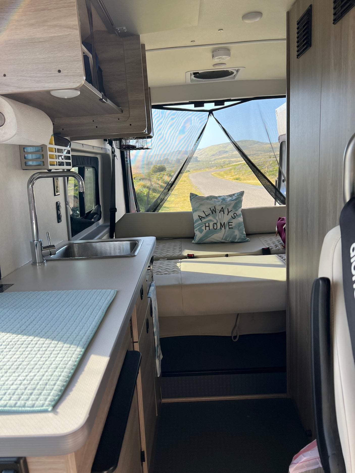 Cozy rv rental interior featuring a practical kitchenette, comfy seating, and a mesh-screened rear door opening to a scenic road.