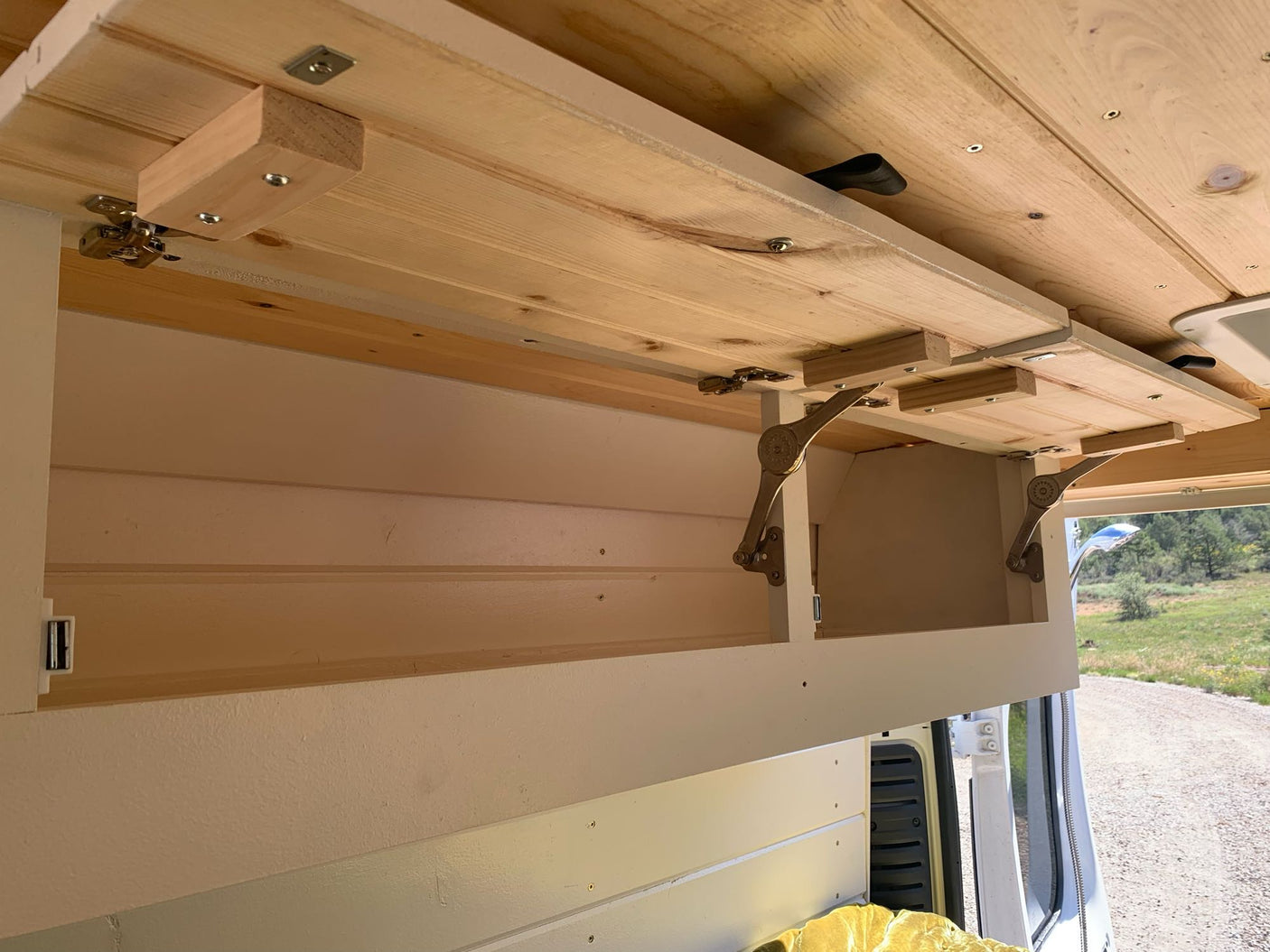 Overhead hinged wooden platform in an RV rental, showing folding support brackets & an open cubby. Perfect for compact living.