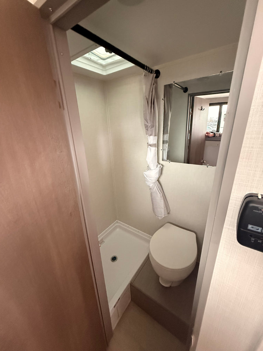 Compact RV rental bathroom with toilet, shower pan, mirror, and skylight overhead for space-saving design.