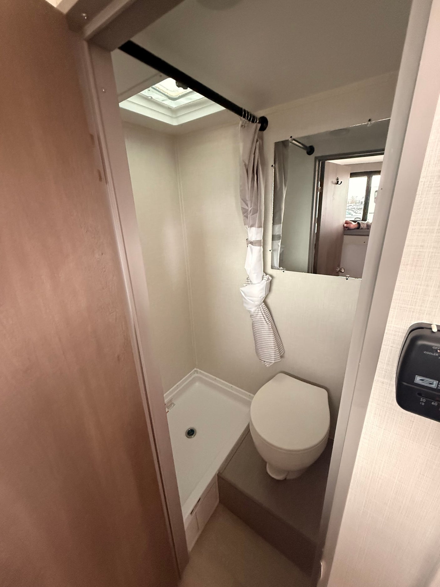 Compact RV rental bathroom with toilet, shower pan, mirror, and skylight overhead for space-saving design.