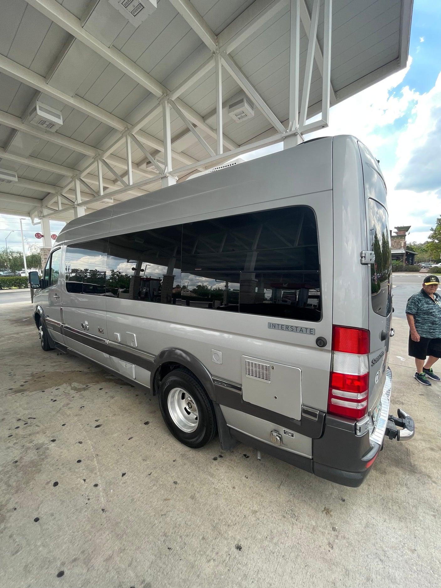 View of a silver Airstream Interstate RV rental at a service station. A person stands near the back of the sleek camper van.