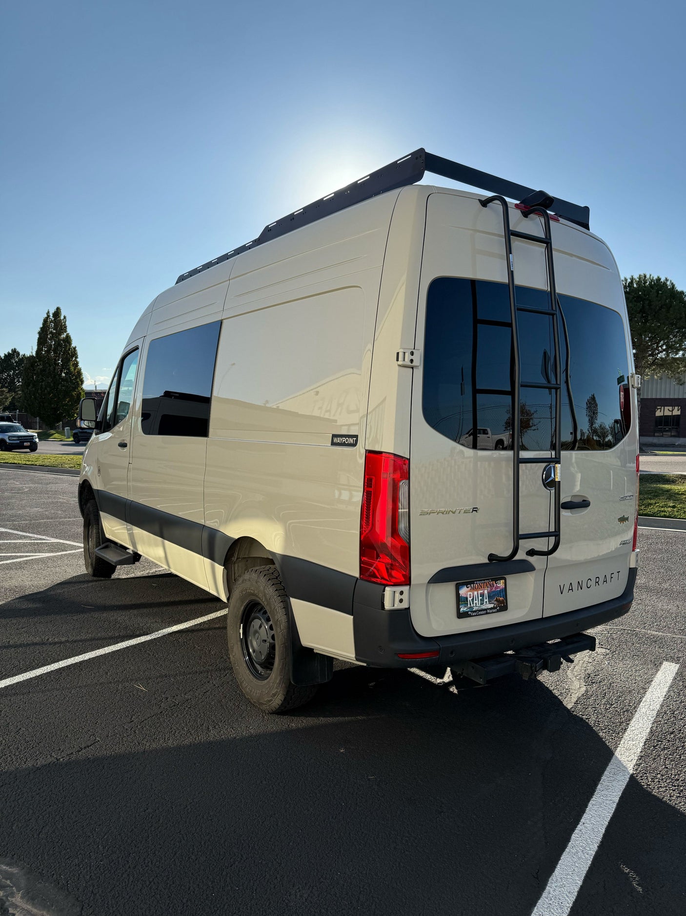 Light-colored Mercedes Sprinter camper van with roof rack, ladder, and AWD, parked outdoors. Perfect for rv rental adventures.
