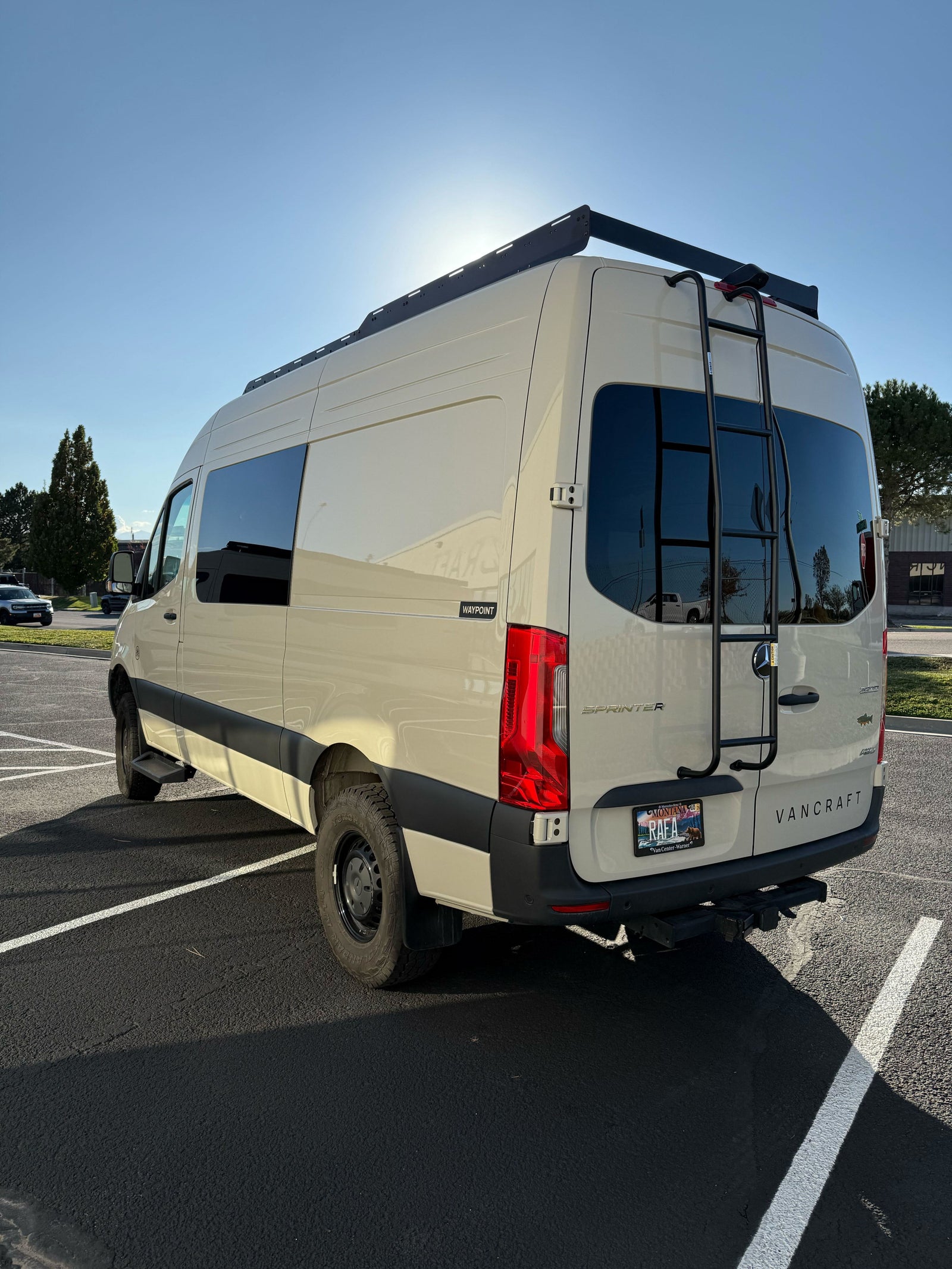 Light-colored Mercedes Sprinter camper van with roof rack, ladder, and AWD, parked outdoors. Perfect for rv rental adventures.