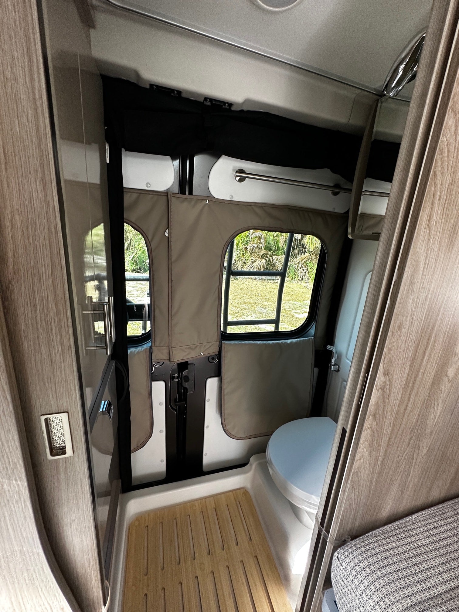 Modern RV rental interior with custom window covers over outdoor views. Features include a sleek kitchen counter and smart storage.