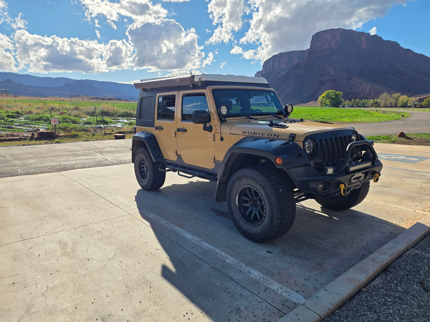 Adventure-ready tan Jeep Wrangler with rooftop tent, great for overlanding or an RV rental, set against scenic mountains.