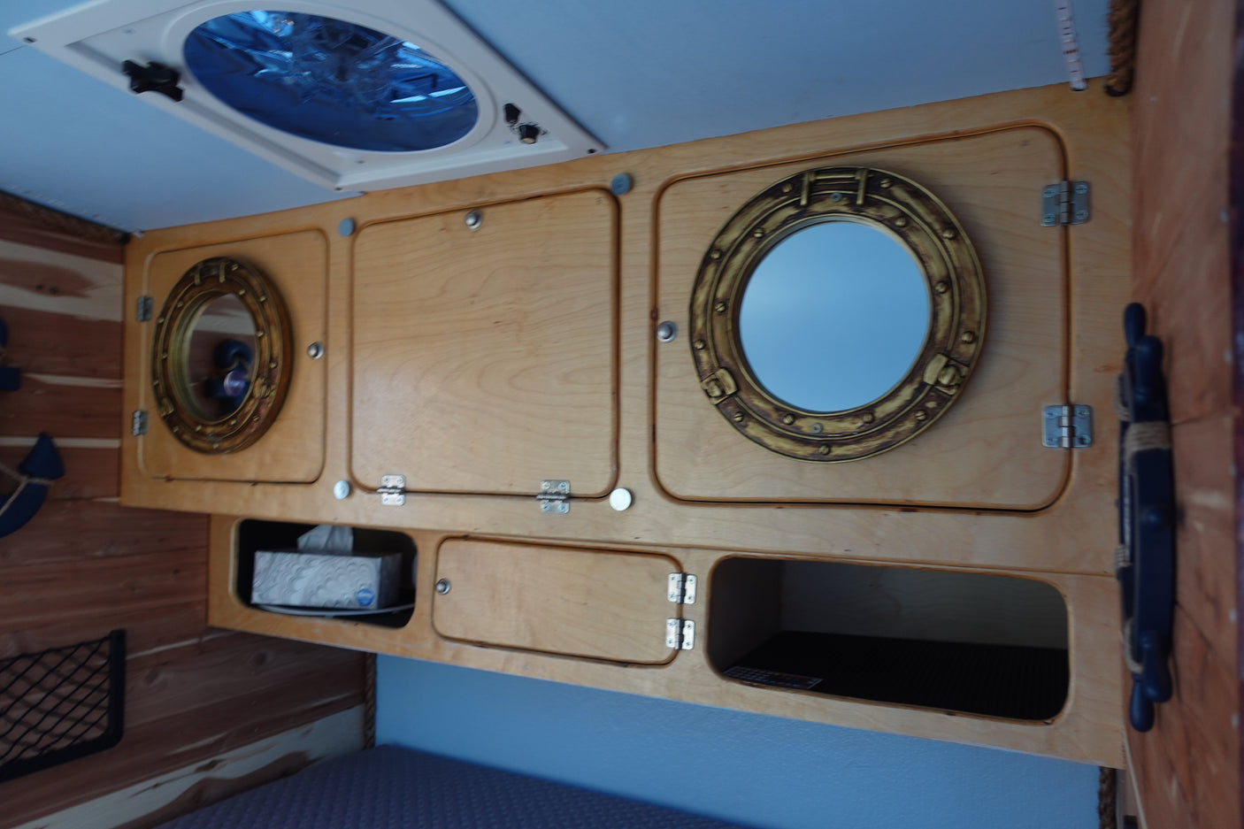 Overhead storage in an RV rental, featuring light wood cabinets with porthole mirrors, a ceiling fan, and nautical decor.
