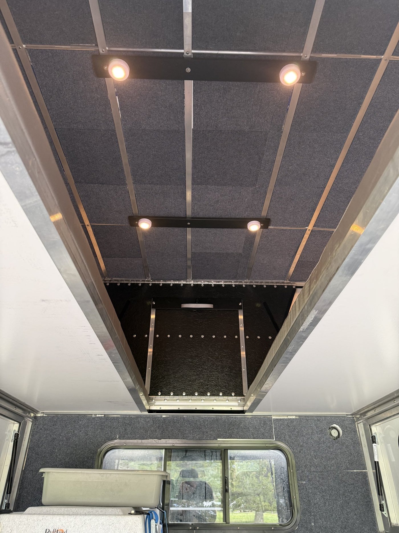 Looking up at the camper ceiling from inside, showing the carpeted insulated ceiling panels, aluminum cross ribs, two dual-LED light bars and the cabover section above the truck cab — photo 5
