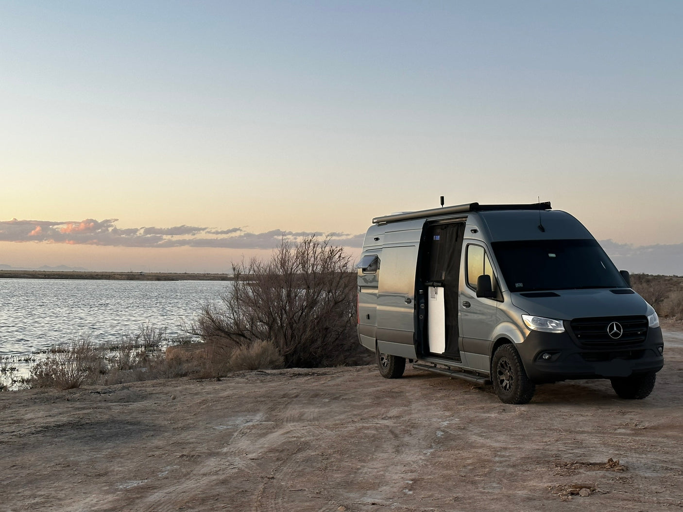 Gray Mercedes-Benz Sprinter RV rental camper van parked by a serene lake at sunset