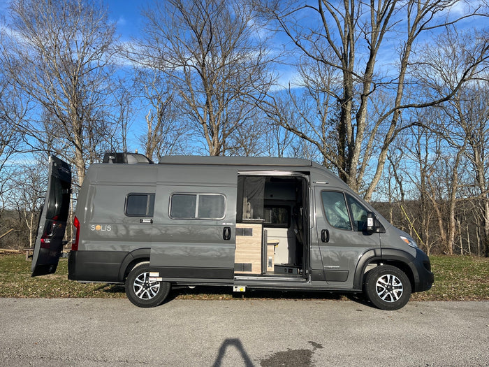 rv rental: A gray Winnebago Solis camper van with open doors, parked outdoors under bare trees on a sunny day.