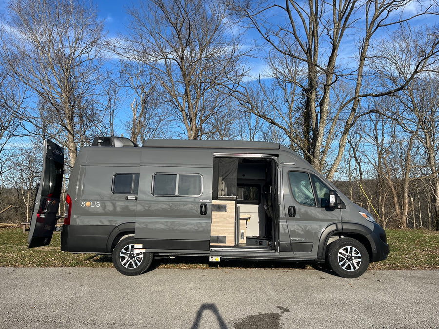 rv rental: A gray Winnebago Solis camper van with open doors, parked outdoors under bare trees on a sunny day.