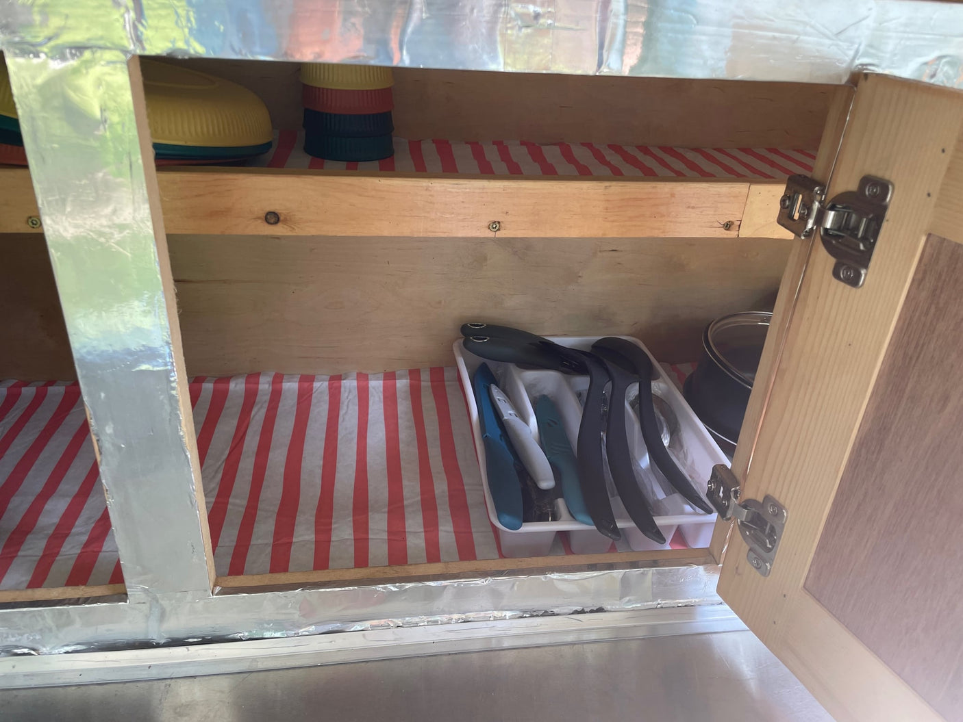 revealing a compact galley with wood and metal storage cabinets.|Cozy RV rental bedroom featuring wooden cabinets