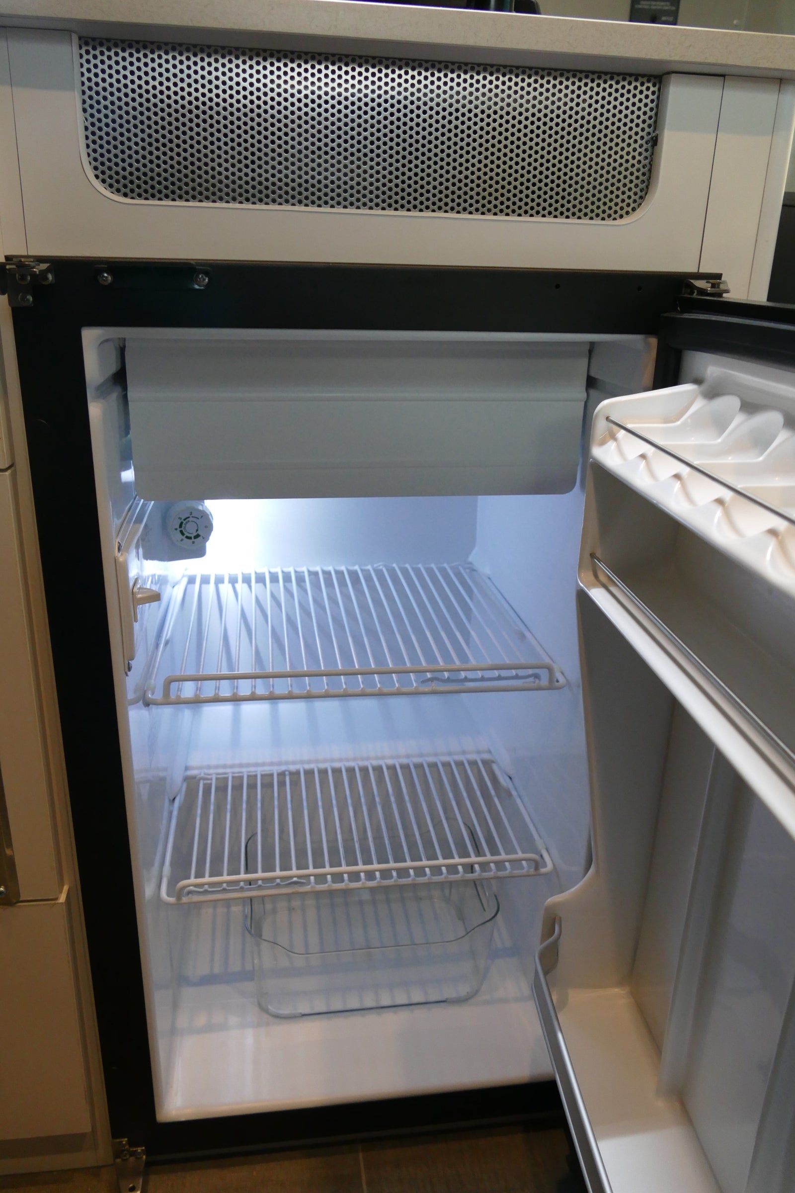 Inside an empty RV rental refrigerator, showing bright interior, wire shelves, and a small freezer.