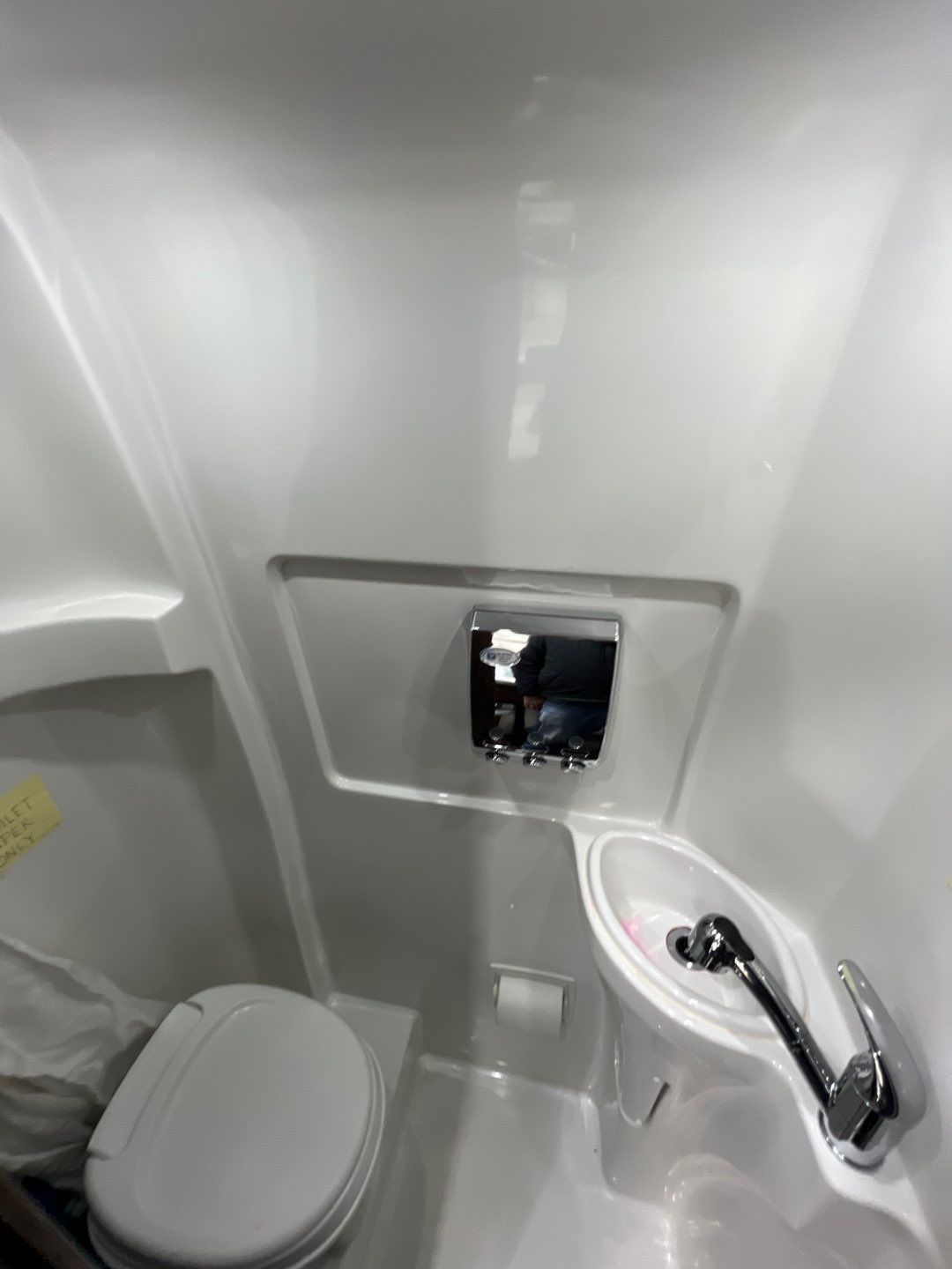 This RV rental's compact wet bath features a white toilet, corner sink with faucet, and chrome wall dispenser. Practical for camper travel.