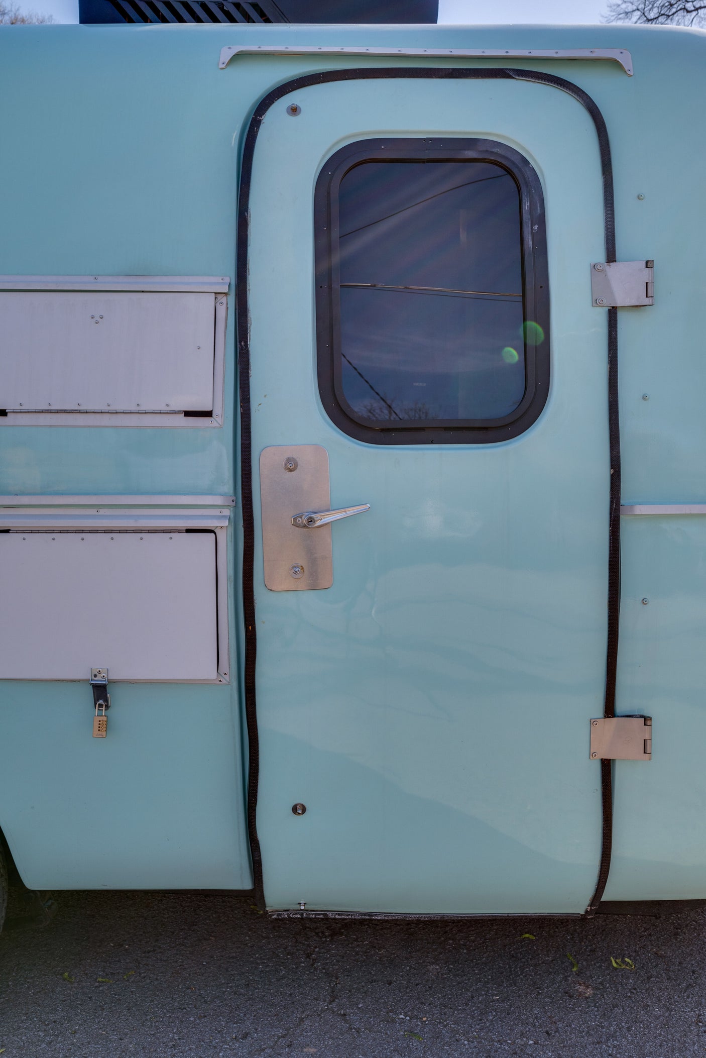Light blue RV rental side showing the entry door with window, handle, and secured storage compartments.