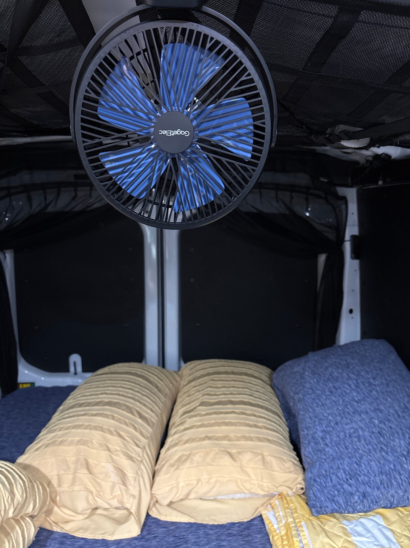 Relax in comfort in this RV rental! Features a bed with yellow pillows, blue blanket, and a cooling ceiling fan.
