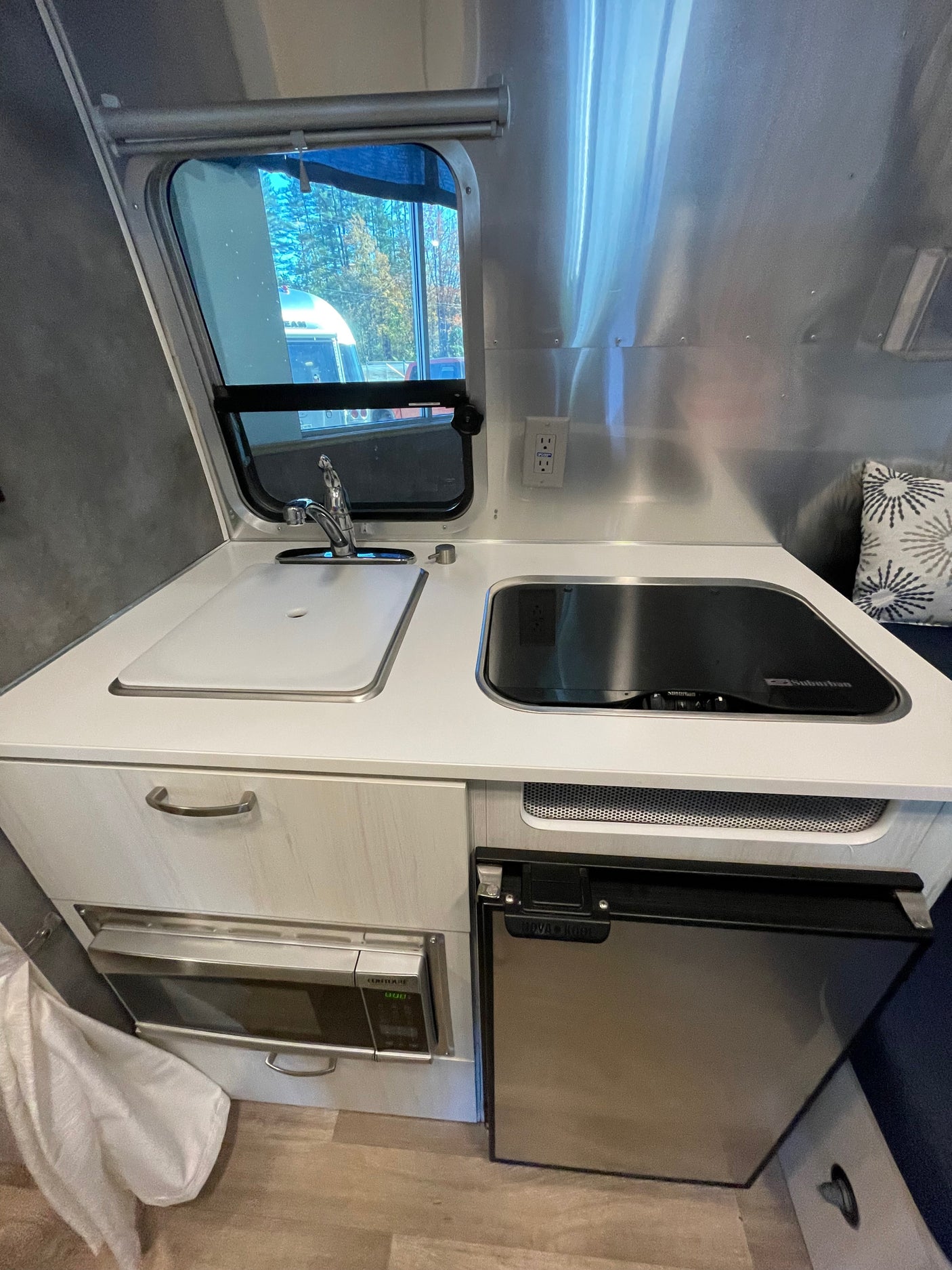 This RV rental's compact kitchen features a sink, cooktop, microwave, and refrigerator, all within a sleek, modern design.