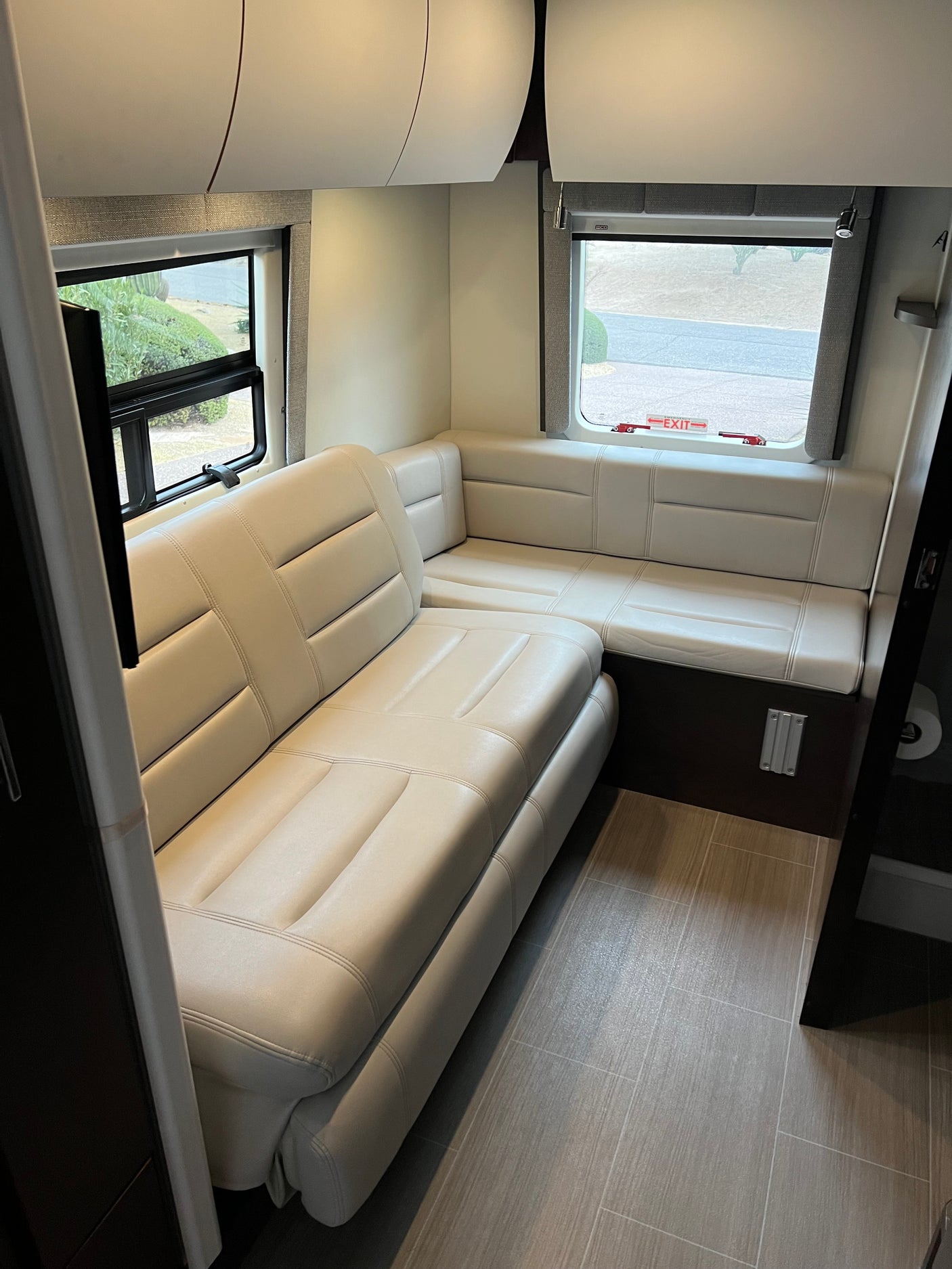 Modern RV rental interior: light L-shaped seating, large windows, and overhead cabinets. Comfortable, compact living space.