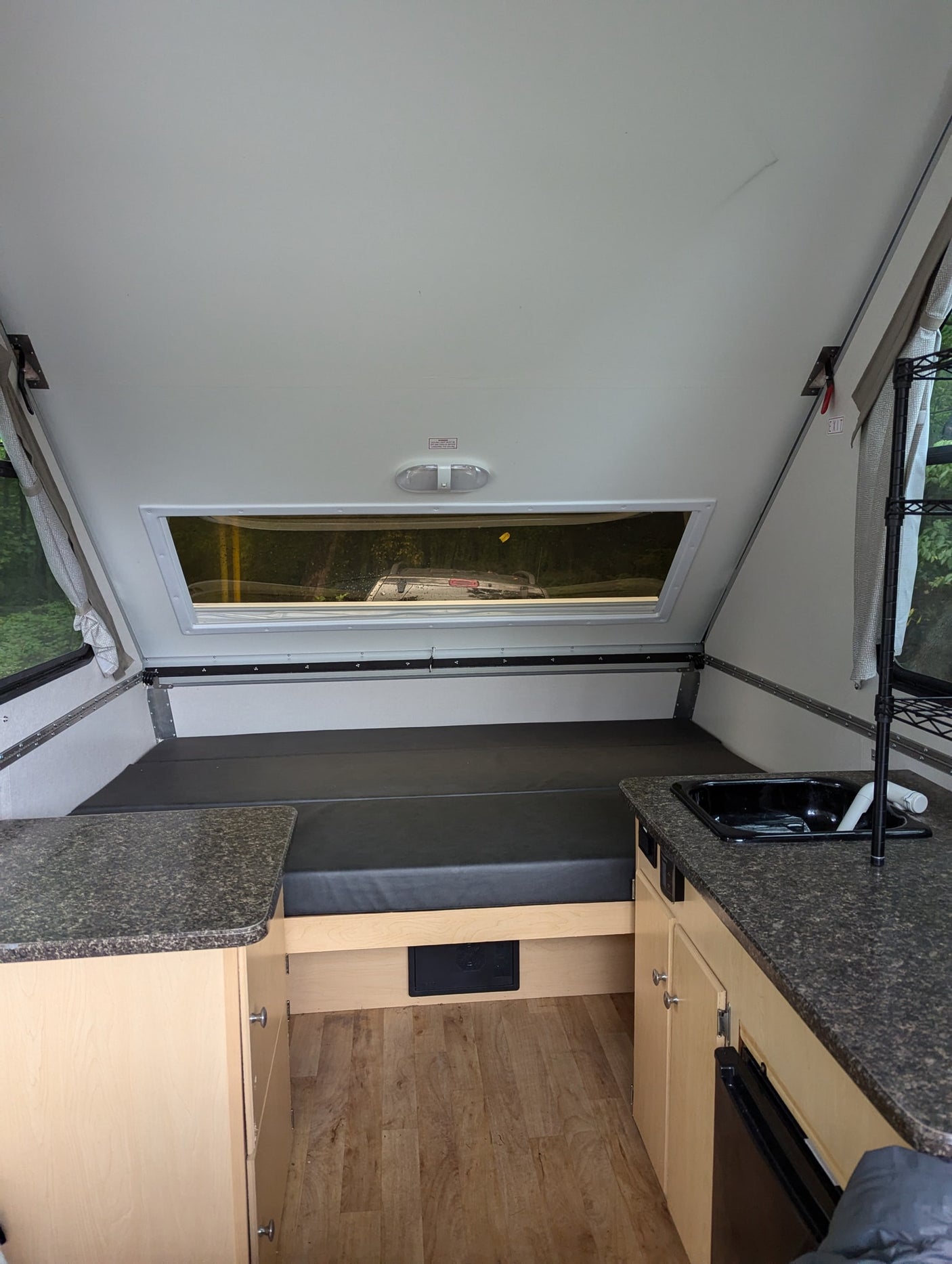 RV rental interior showing a bed, kitchen counter with sink, and wood storage cabinets. Bright, compact space.