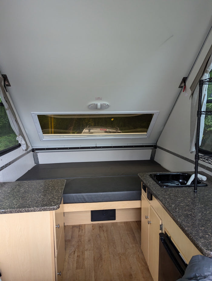 RV rental interior showing a bed, kitchen counter with sink, and wood storage cabinets. Bright, compact space.