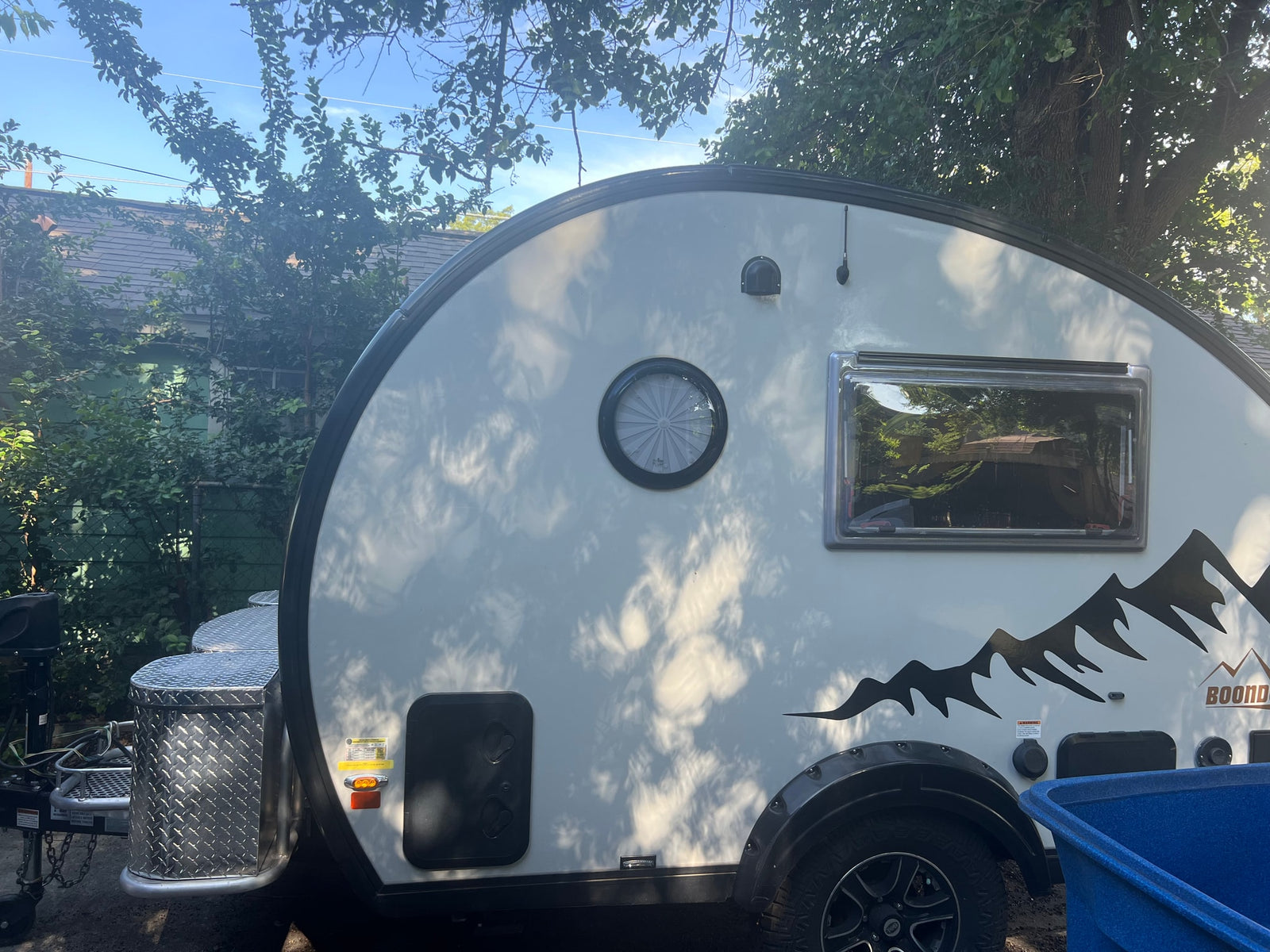 A white Boondock travel trailer, ideal for RV rental adventures. Features mountain graphics, a round window, and storage box.