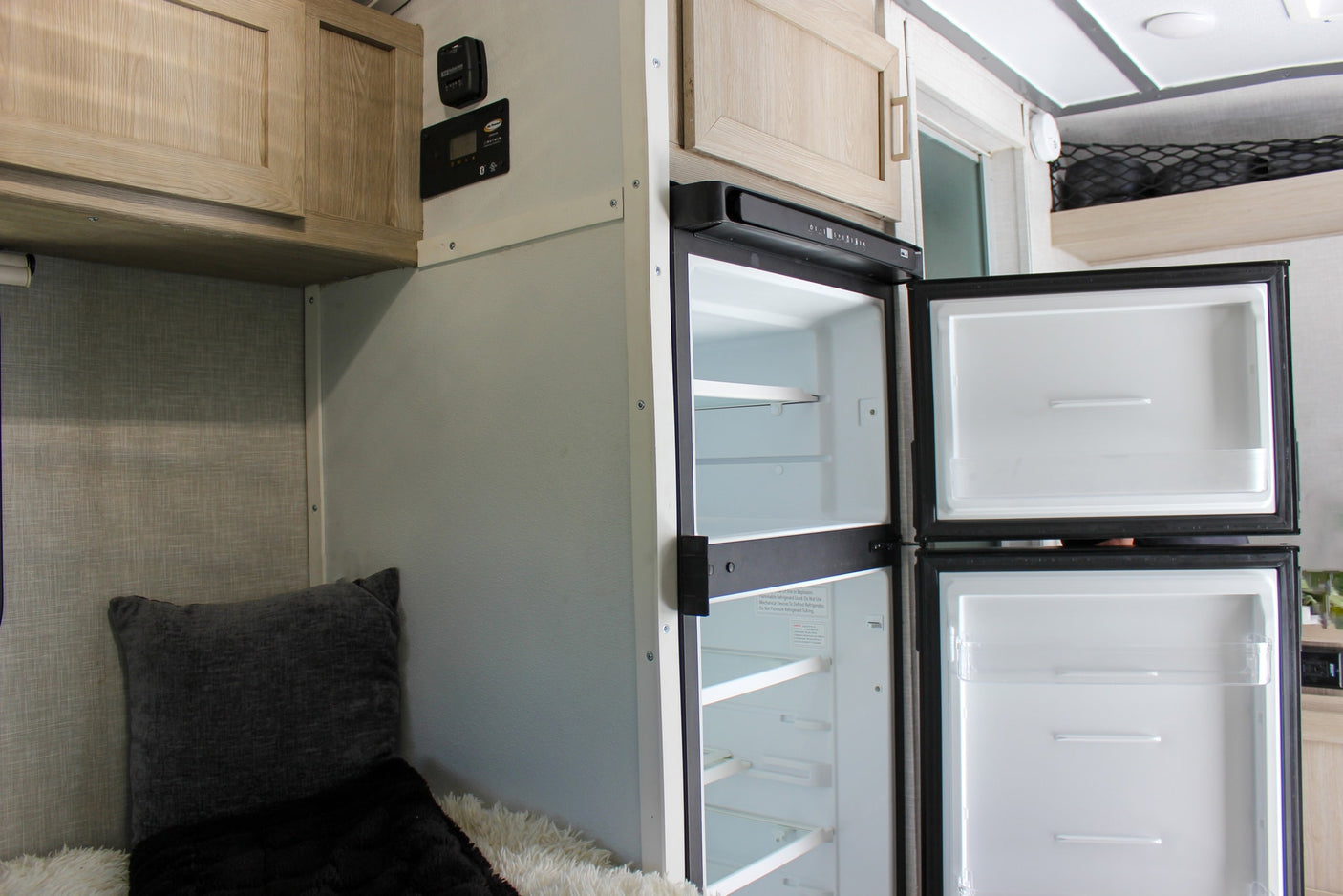 Empty fridge & freezer inside an RV rental, ready for your provisions. Features cabinets & control panel for an adventure.