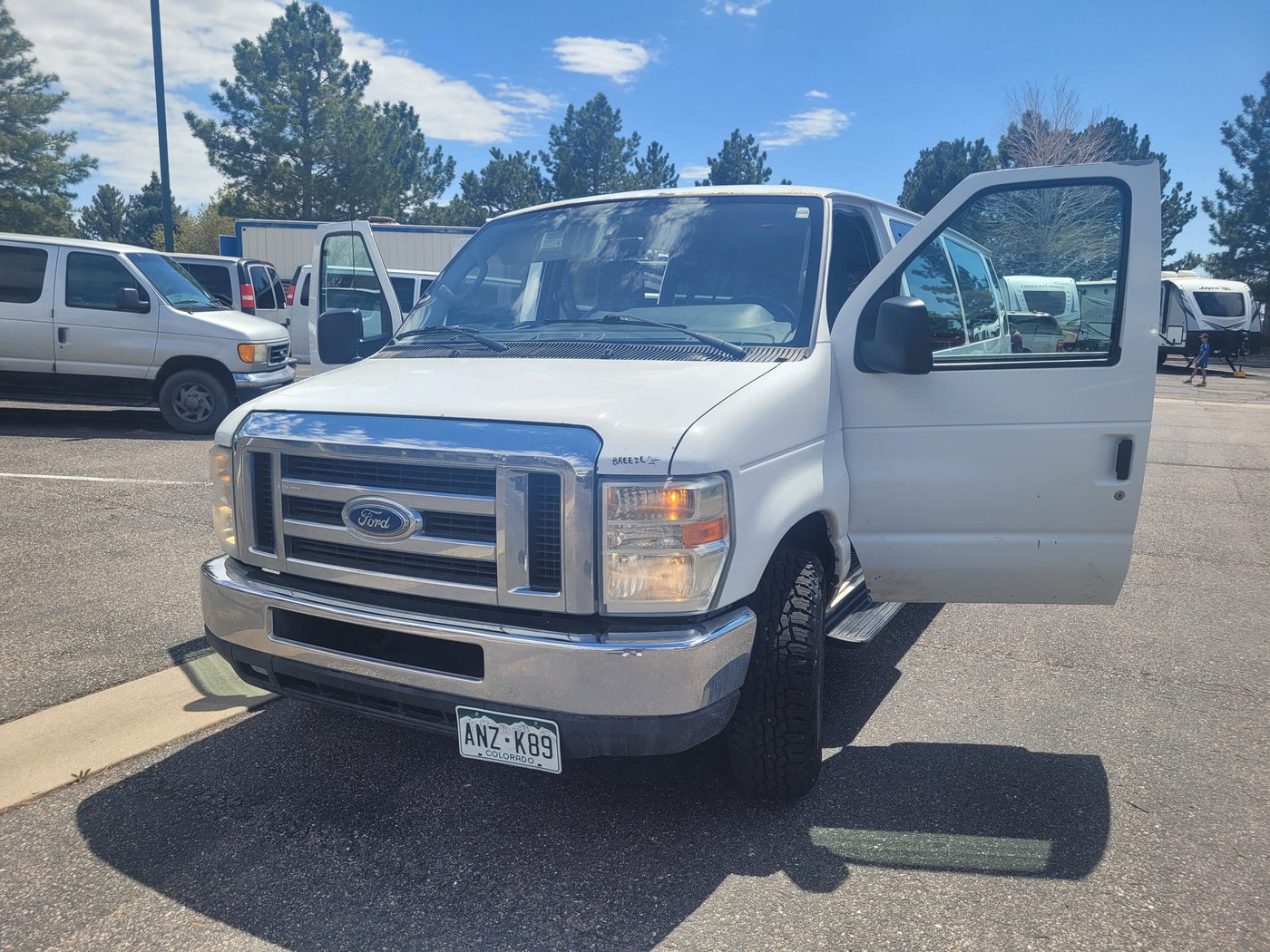 White Ford van with open door, parked at an RV rental lot with travel trailers. Colorado license plate ANZ-K89. — photo 1