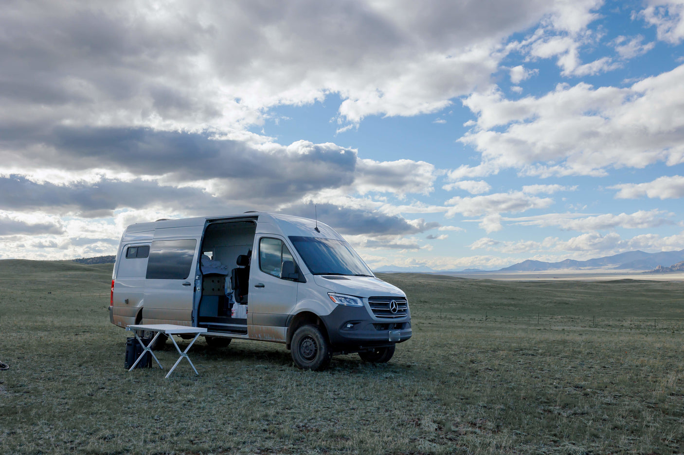 This Mercedes-Benz Sprinter RV rental in a vast grassy landscape under a cloudy sky is perfect for outdoor adventure & van life camping.