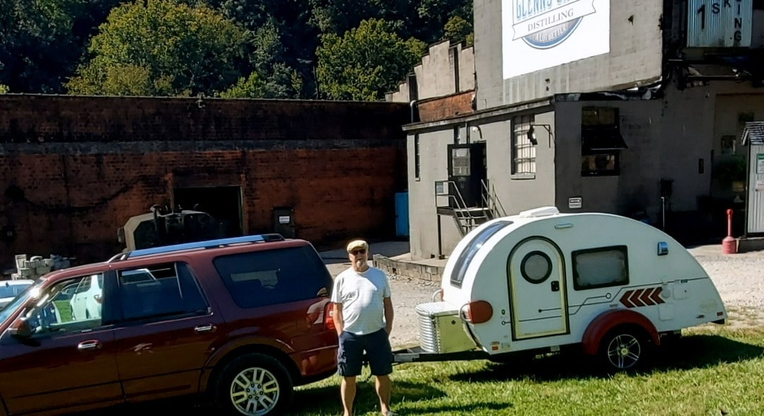 Man with his SUV and a compact 'rv rental' teardrop camper by a distillery