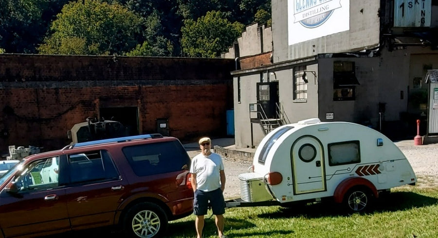 Man with his SUV and a compact 'rv rental' teardrop camper by a distillery