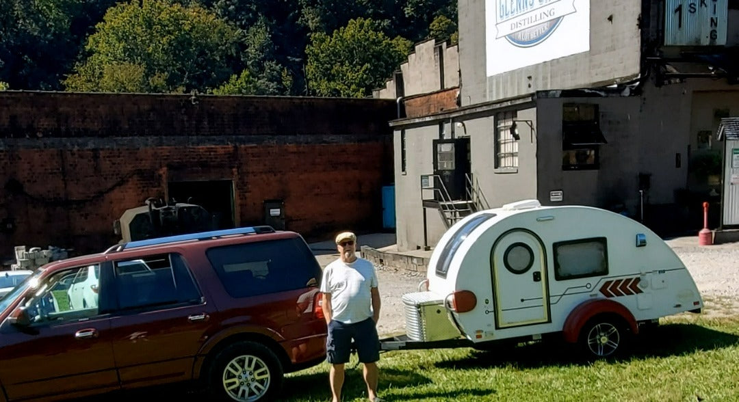 Man with his SUV and a compact 'rv rental' teardrop camper by a distillery