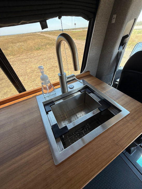 RV rental's compact kitchenette: stainless steel sink with a colander insert, gooseneck faucet, and soap on wood countertop.