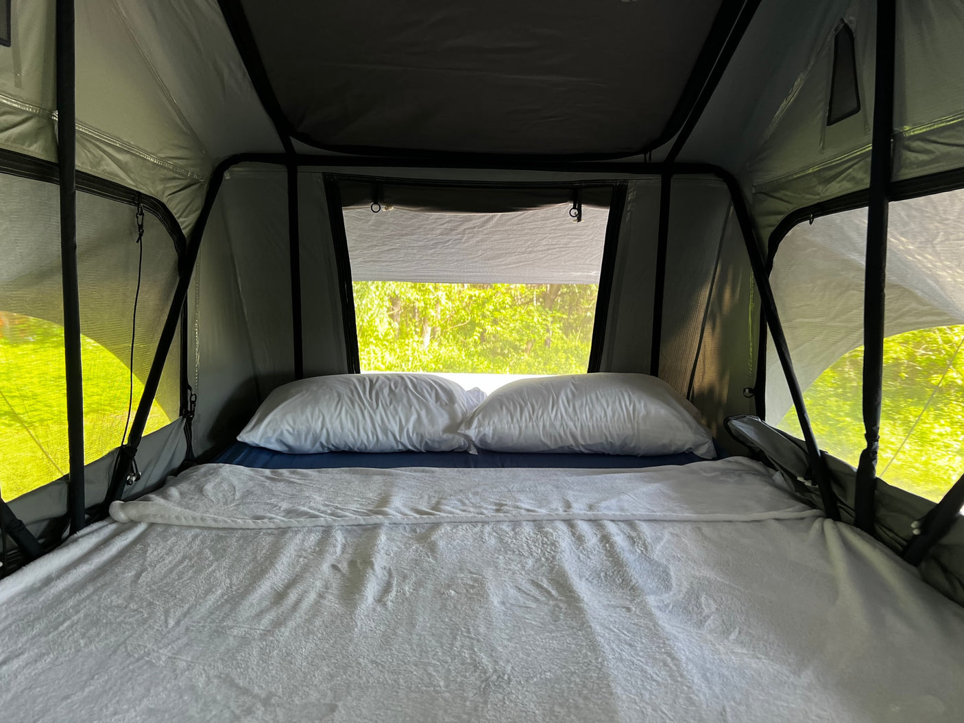 A comfy bed inside a modern roof-top tent, perfect for an rv rental adventure amidst green nature.