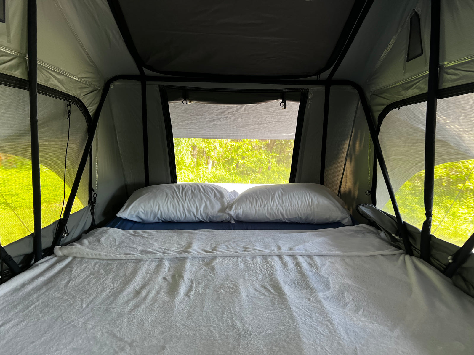 A comfy bed inside a modern roof-top tent, perfect for an rv rental adventure amidst green nature.
