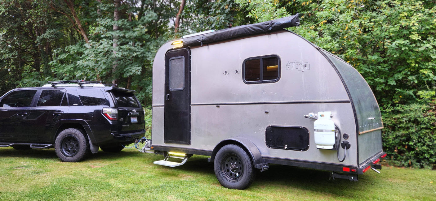 Black SUV hitched to a silver teardrop RV camper, ready for adventure. Explore nature with an RV rental!