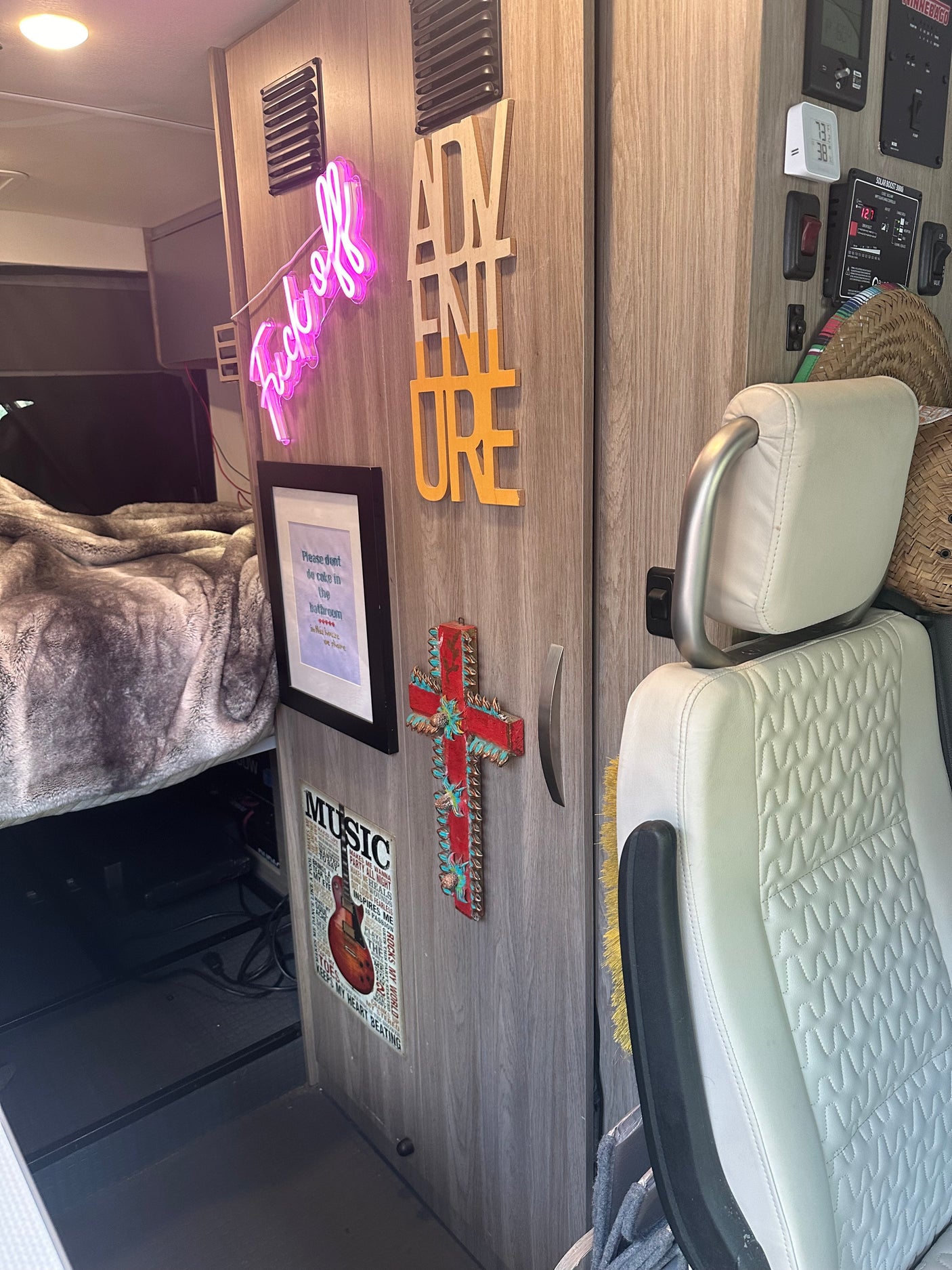 RV rental interior features unique decor: "Fuck off" neon, "ADVENTURE" sign, guitar art, and a cozy bed area.