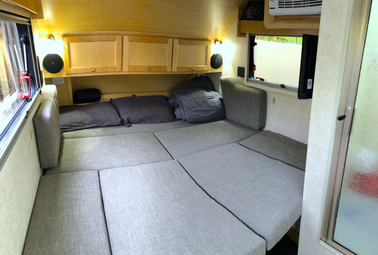 RV rental: Compact interior showing a comfy convertible bed, wood cabinets, and air conditioning unit. Ready for adventures!