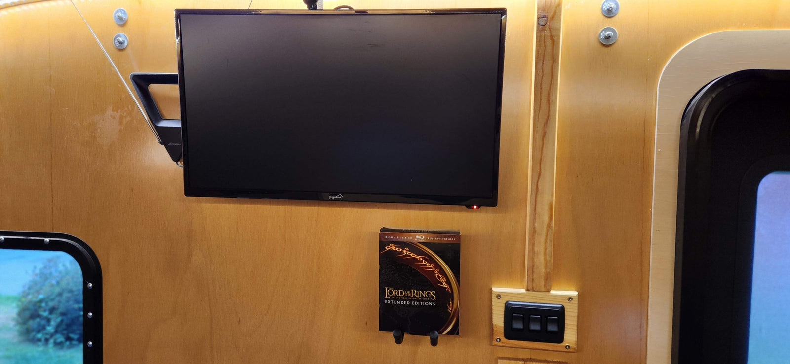 RV rental interior: A TV mounted on wood, Lord of the Rings Blu-rays below, and control switches to the right.