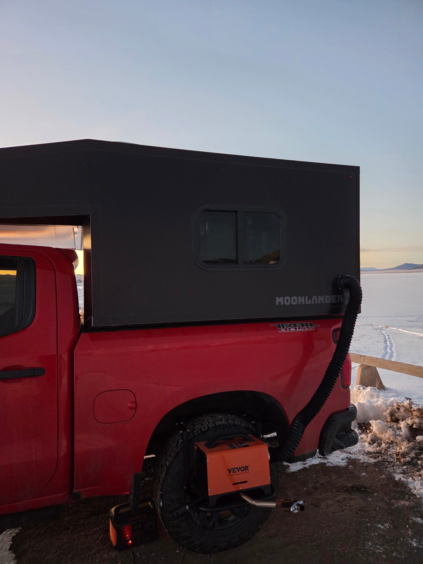 Red pickup with a black Moonlander truck camper, Vevor heater, and Jackery power in snow. Perfect for an RV rental adventure.