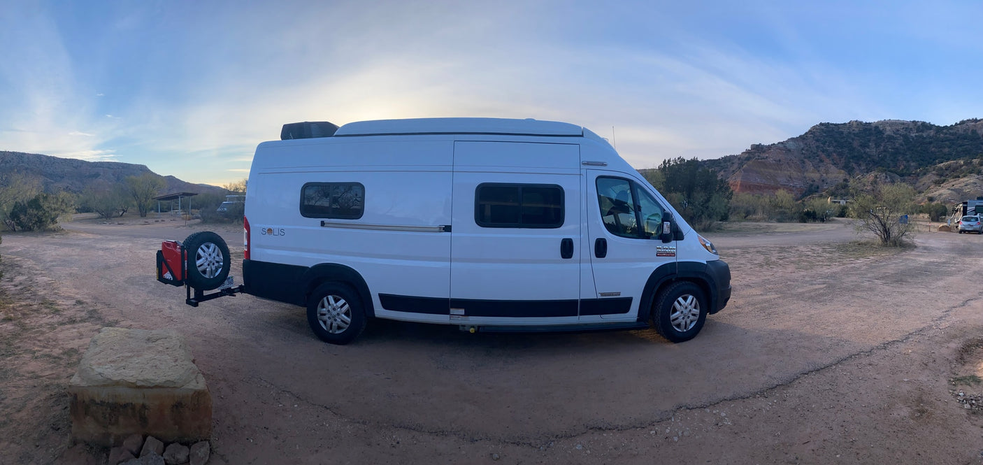 open field under a clear blue sky with distant hills.|This Winnebago Solis RV rental is perfectly parked at a scenic desert campsite