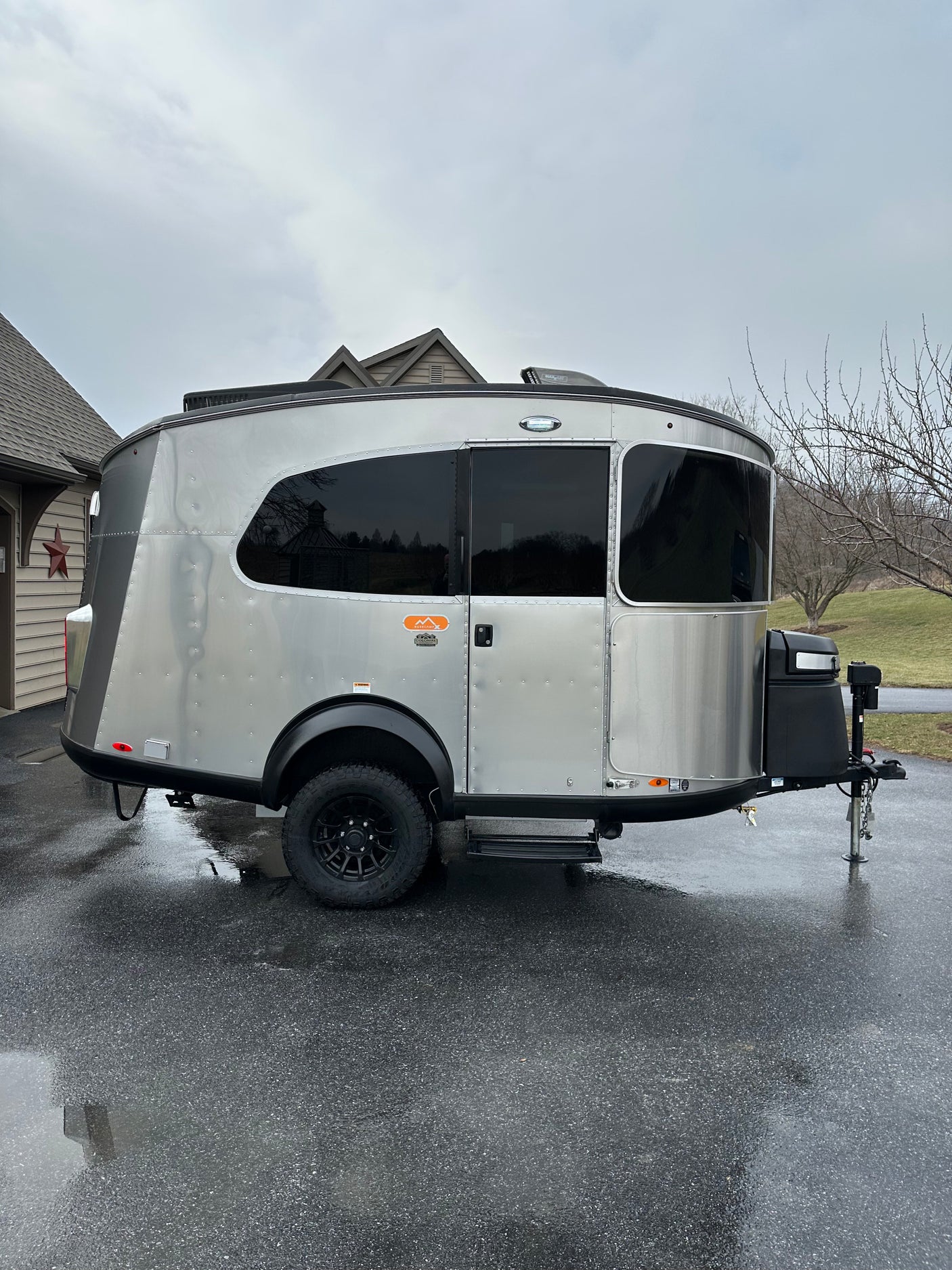 Stylish Airstream Basecamp travel trailer, silver with black accents, on wet driveway. Ideal for rv rental adventures.