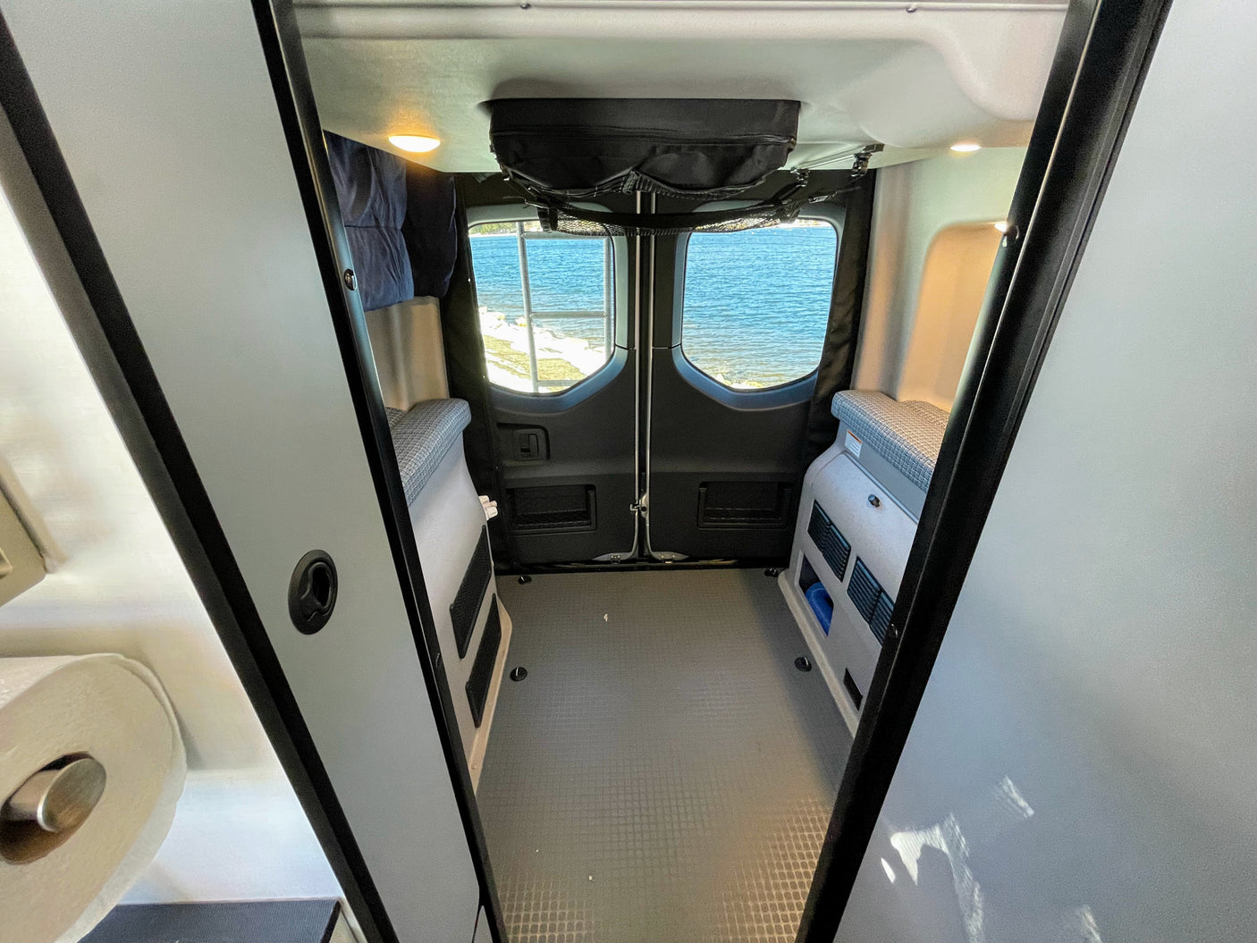 Explore with this RV rental! Inside a camper van, enjoy a water view from the rear windows, with modular interior and storage.