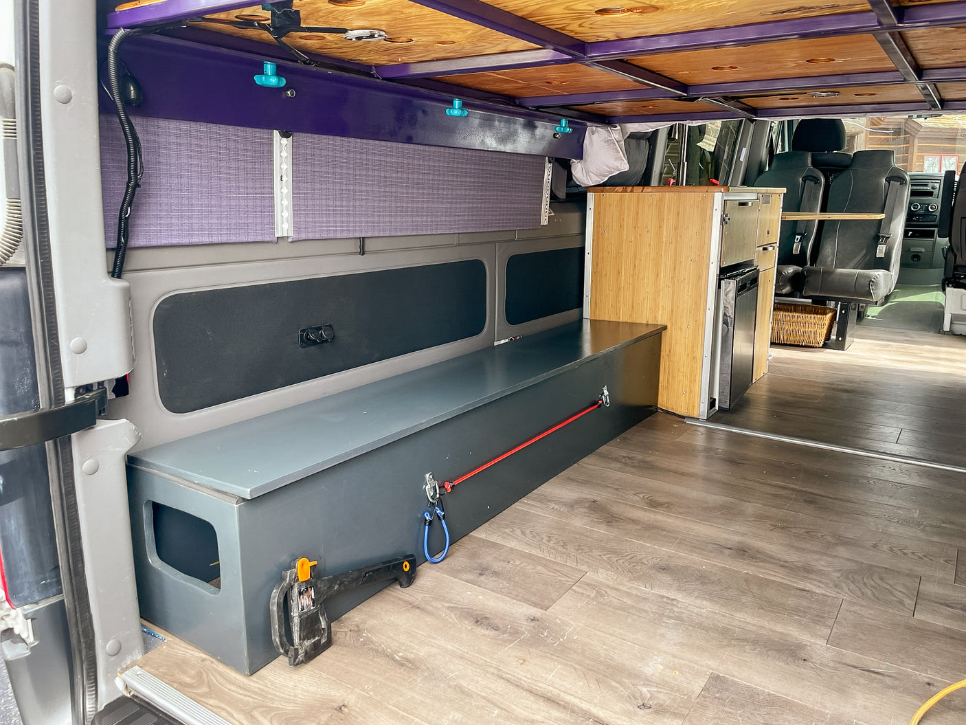 RV rental interior: custom storage bench, compact kitchen, wood floor, and overhead bed structure for travel.