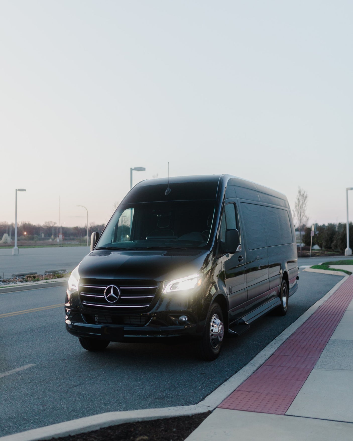 A black Mercedes-Benz Sprinter van with bright headlights, on a road. A versatile option for luxury travel or your next RV rental.
